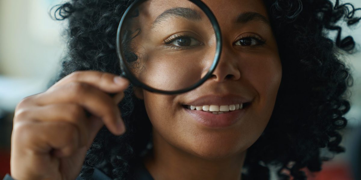 Beautiful curly smiling multiracial woman looking through magnifying glass